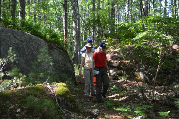 Hikers file through a narrow section of trail between boulders and ledge.