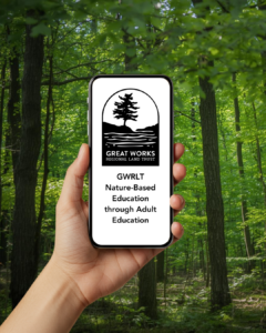 Picture of someone holding up a cellphone in the forest with GWRLT logo ont he screen